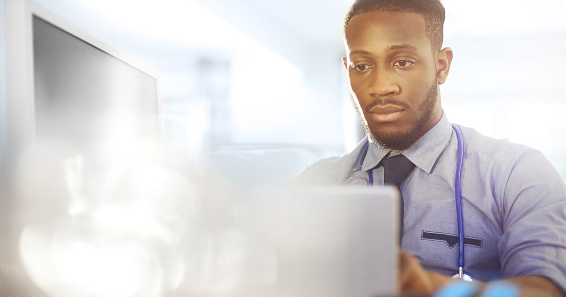 Man wearing a stethoscope around his neck looking at a laptop